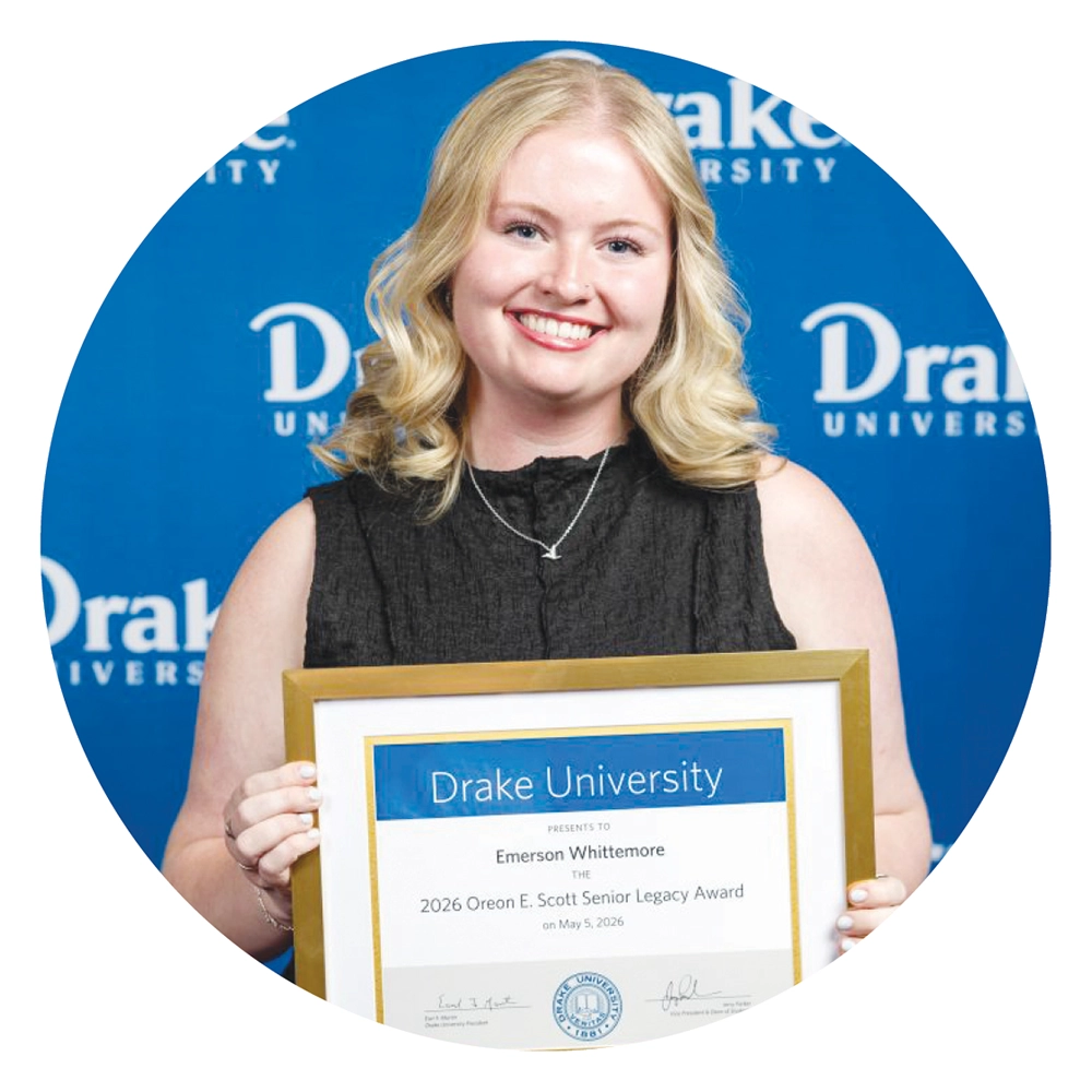 Emerson Whittemore holds a framed Drake University award certificate in front of a blue backdrop.