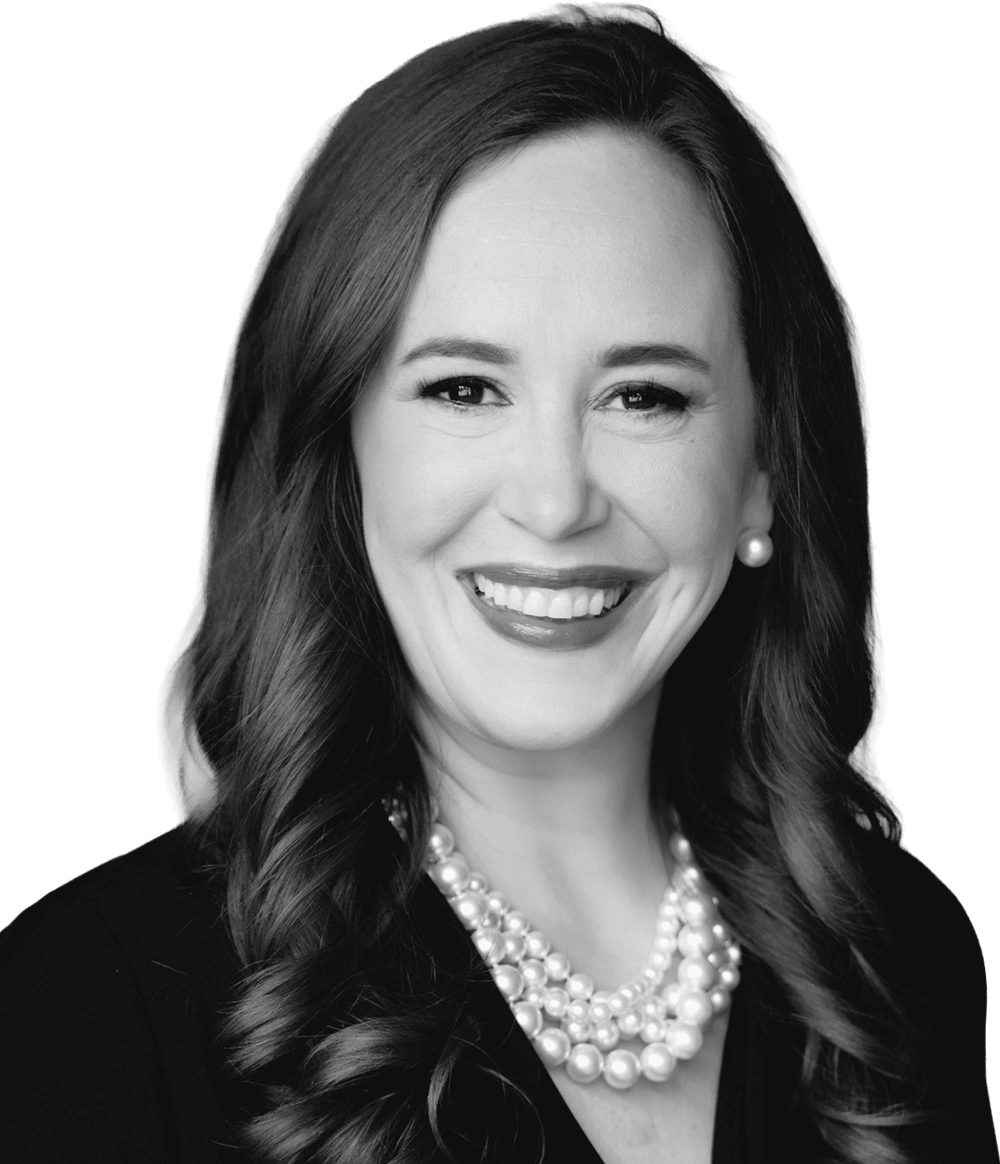 Black-and-white portrait of a smiling Erica Axiotis with long wavy hair wearing a multi-strand pearl necklace.