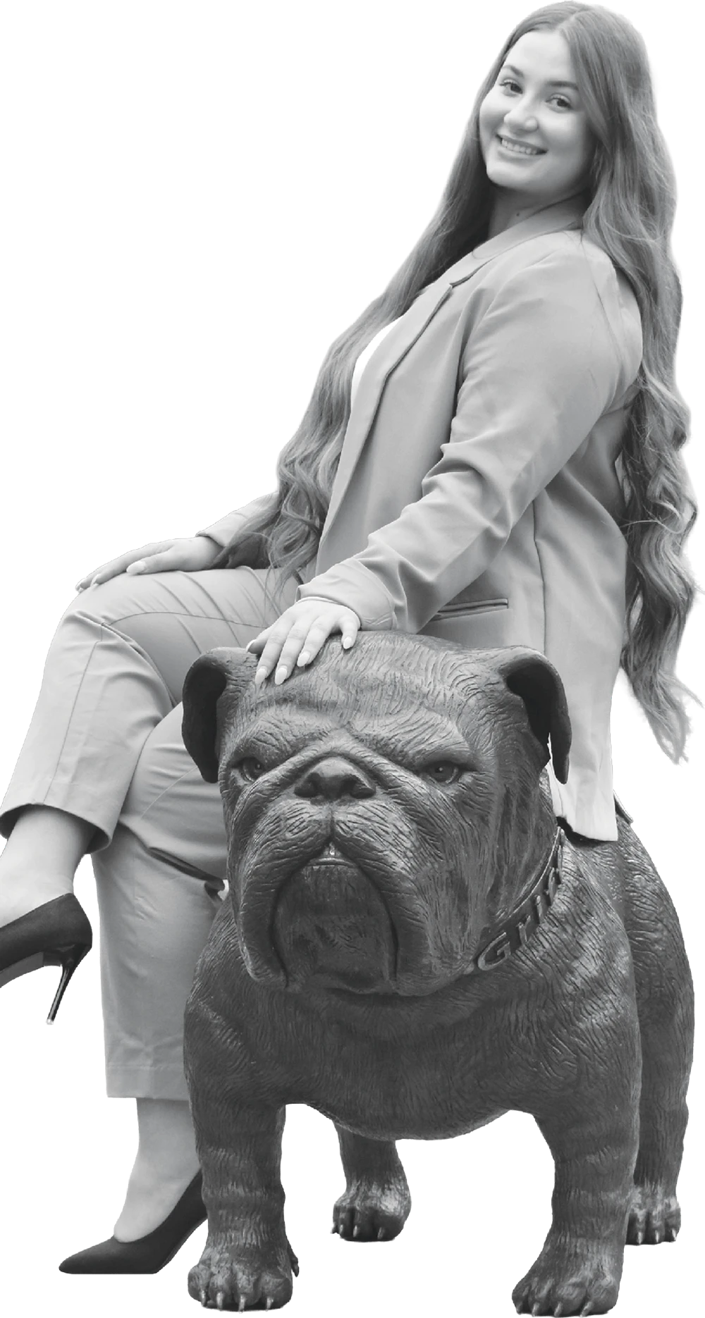 Black-and-white photo of a smiling Samra Aksamovic in a suit sitting next to a bronze bulldog statue.