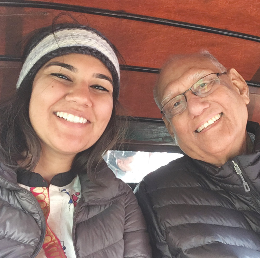 A smiling young woman wearing a headband takes a selfie with an older man in glasses in a vehicle.