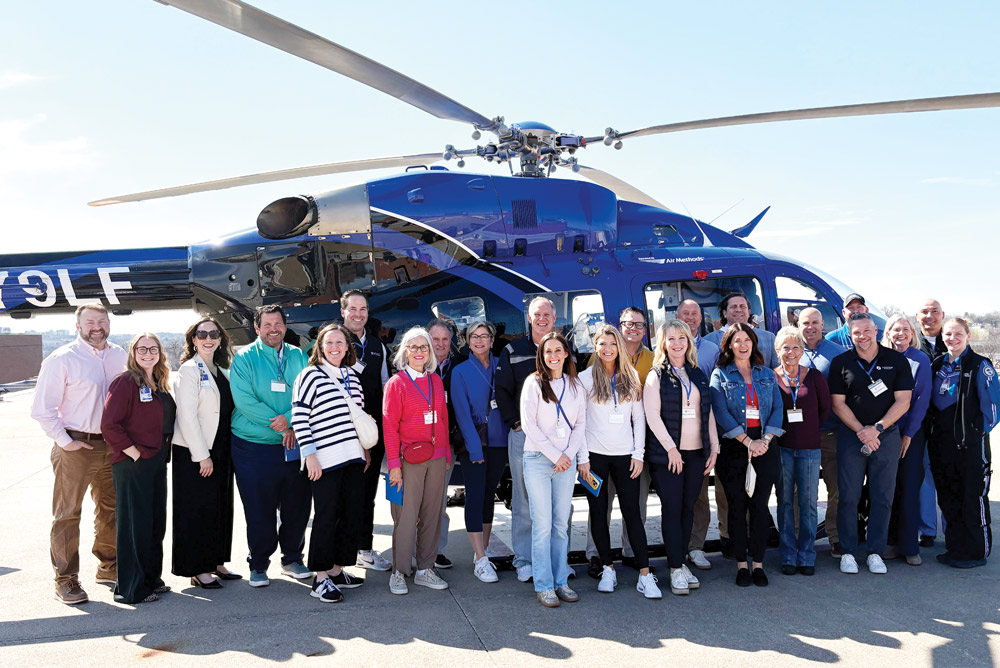 A group of people poses together on a helipad in front of a blue medical transport helicopter.
