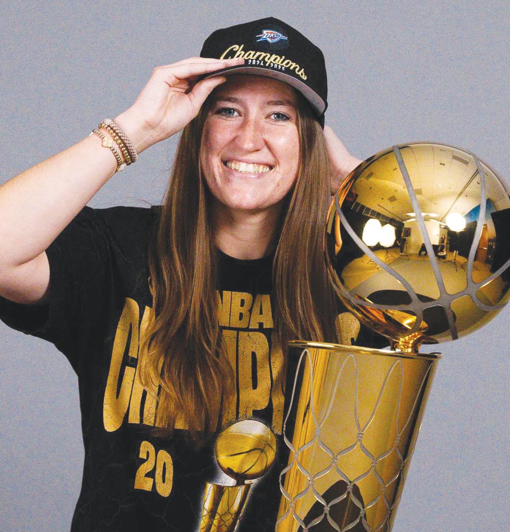 Kendall Hunt wearing an NBA Champions hat poses while holding a large gold Larry O'Brien trophy.