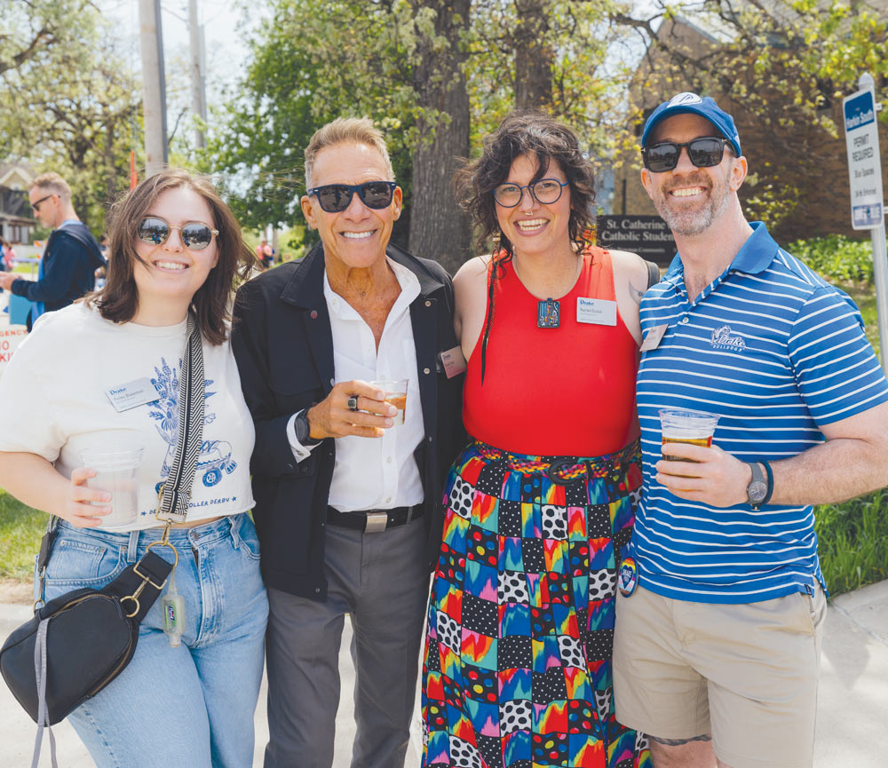 Four alumni pose outdoors in sunglasses while holding drinks at an alumni gathering event.