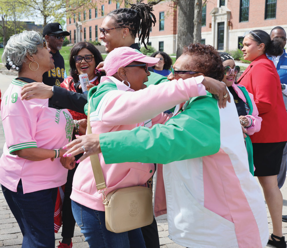 Members of Alpha Kappa Alpha sorority warmly hug and greet each other outdoors at a gathering.