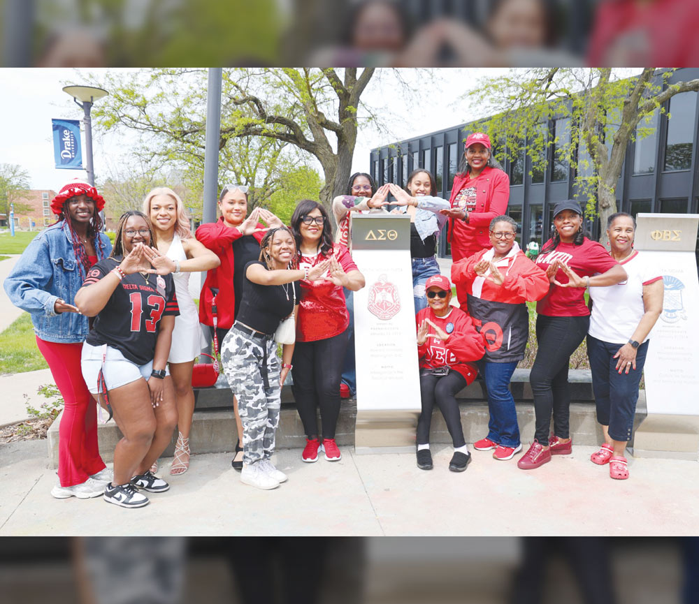 Members of Delta Sigma Theta sorority dressed in red and white pose around a campus fraternity monument.