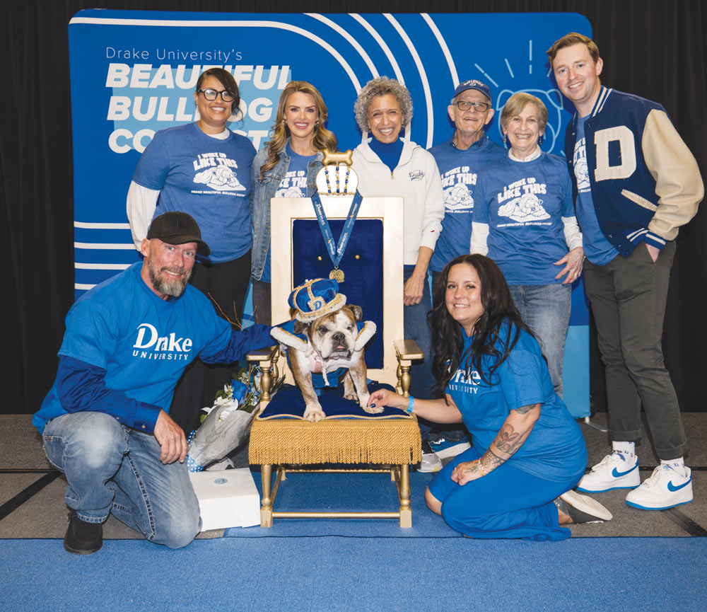 Group poses around an English bulldog wearing a crown while seated on a throne during a contest.